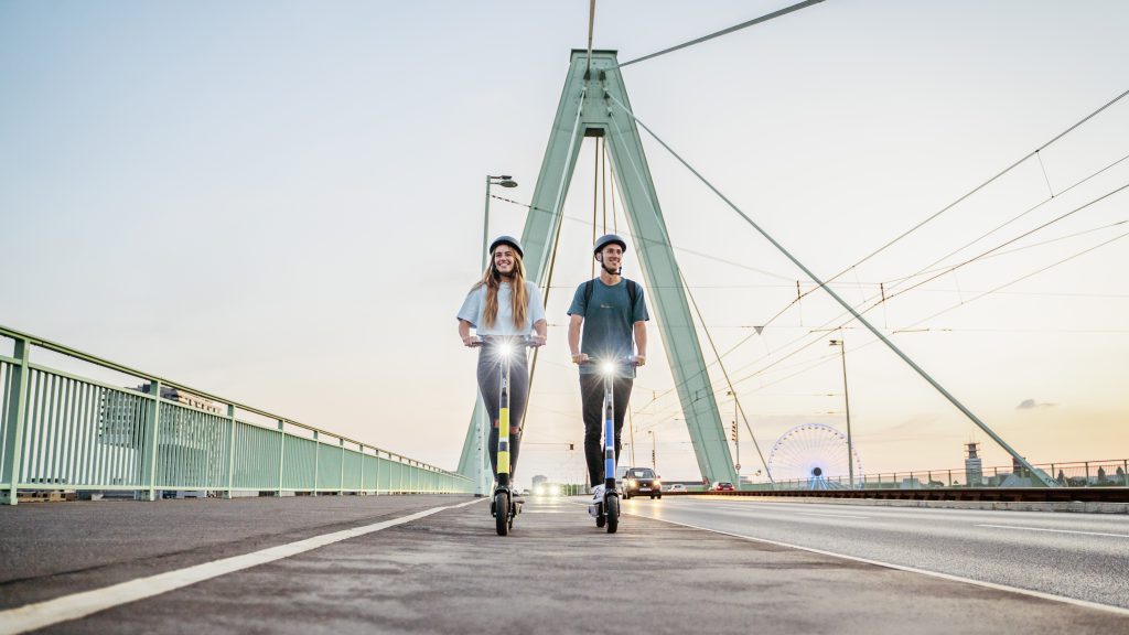 A picture of a woman and a man riding Dott scooters next to each other on a bridge.
