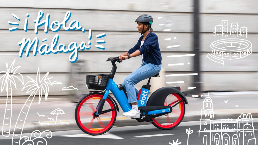 En la cabecera hay la imagen de una mujer circulando con una bici eléctrica Dott de color azul. El sol se refleja en la acera. El fondo está borroso para indicar que se está moviendo. En el fondo se puede ver la ilustración de una silueta urbana en color blanco.